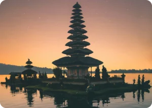 A peaceful Balinese temple sits on a reflective lake at sunset, representing the spiritual and cultural depth showcased by Coco Development Group in their Bali culture guide.
