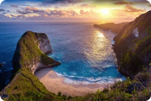 A golden sunset over Kelingking Beach on Nusa Penida, Bali, with clear skies and calm waters, illustrating Coco Development Group’s guide on the best times to visit Bali.
