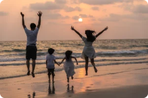 A joyful family jumps along the shore at sunset, reflecting the kind of memorable moments Coco Development Group highlights in their guide to family-friendly attractions in Bali.