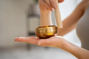 A person gently holding and playing a Tibetan singing bowl during a calming session, symbolizing the peaceful practices at Coco Development Group’s yoga retreats for beginners in Bali.
