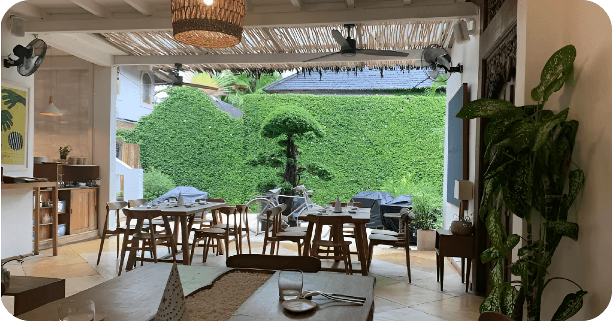 Airy dining room with wooden tables overlooking leafy garden wall