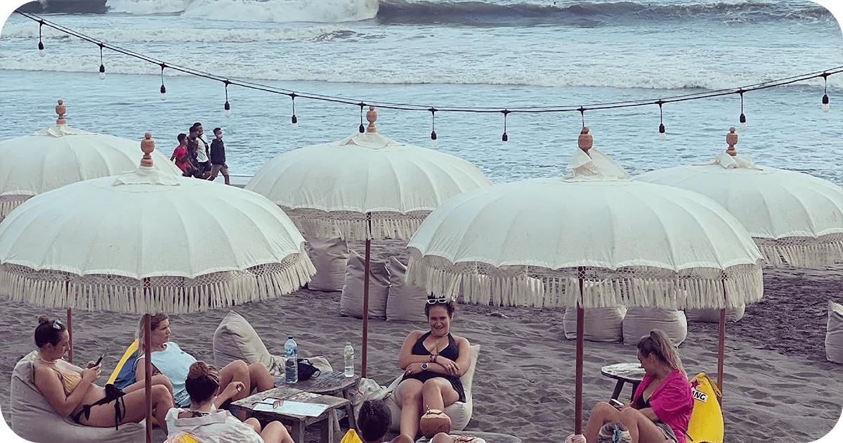 Beach setup with white parasols, beanbags, and overhead string lights