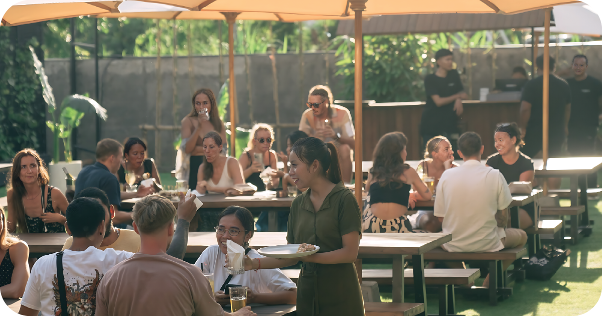 Busy beer garden with umbrellas, communal benches, and table service