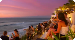 Cliffside bar seating facing pink sunset over the ocean