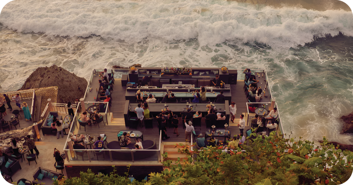 Clifftop deck bar packed with patrons beside crashing waves