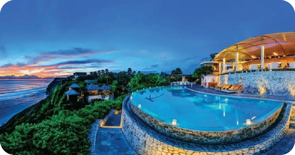 Clifftop infinity pool beside illuminated restaurant at sunset
