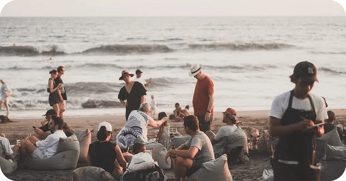 Crowded beach lounge on beanbags with ocean backdrop and servers