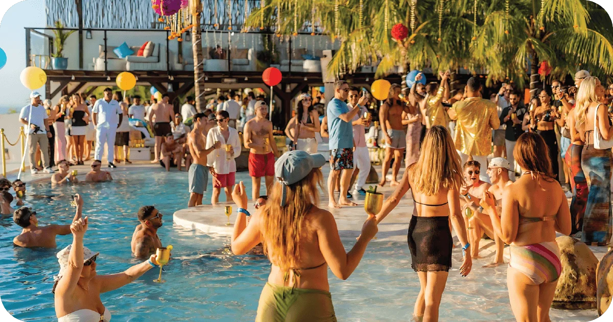 Daytime pool party with palm trees and crowd holding cocktails