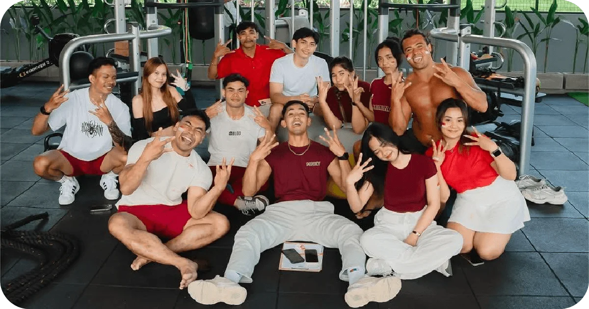 Group sitting on gym floor after workout, machines behind