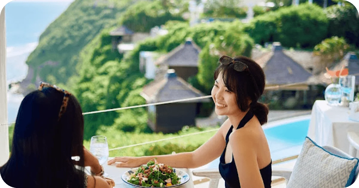 Guests dining with salad beside ocean-view pool and greenery