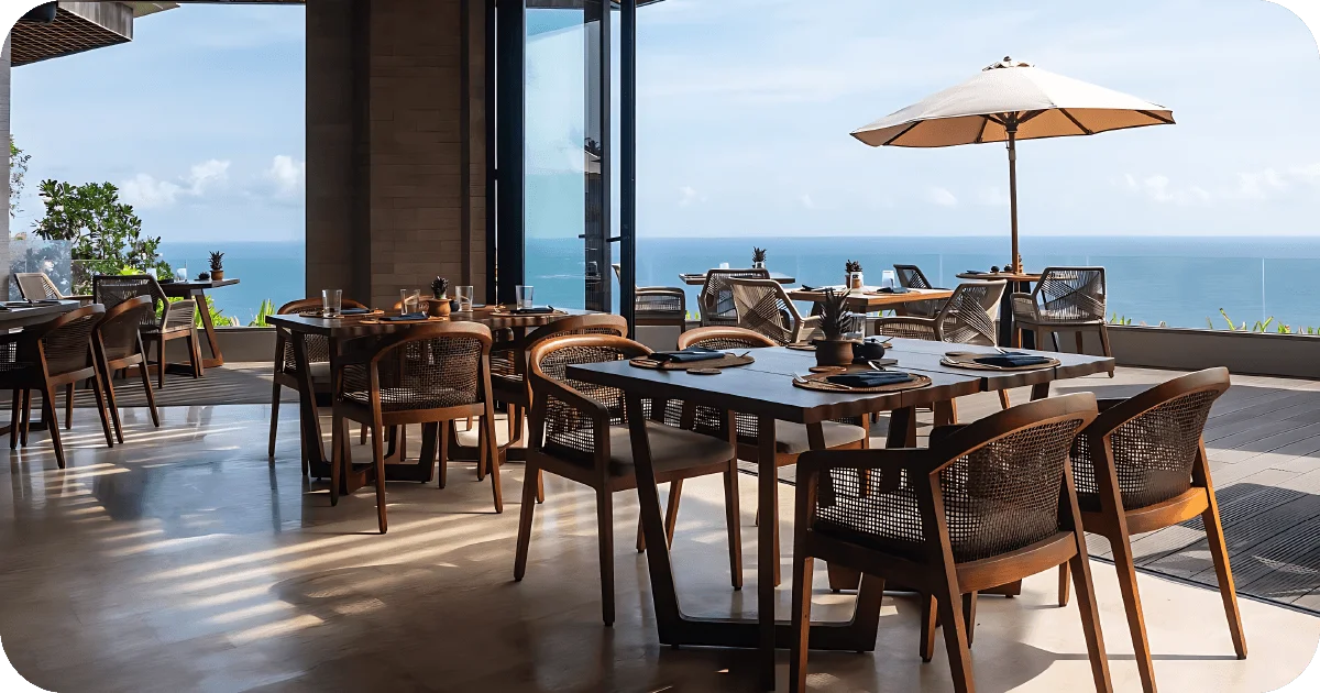 Indoor–outdoor dining facing ocean, wooden tables and umbrellas