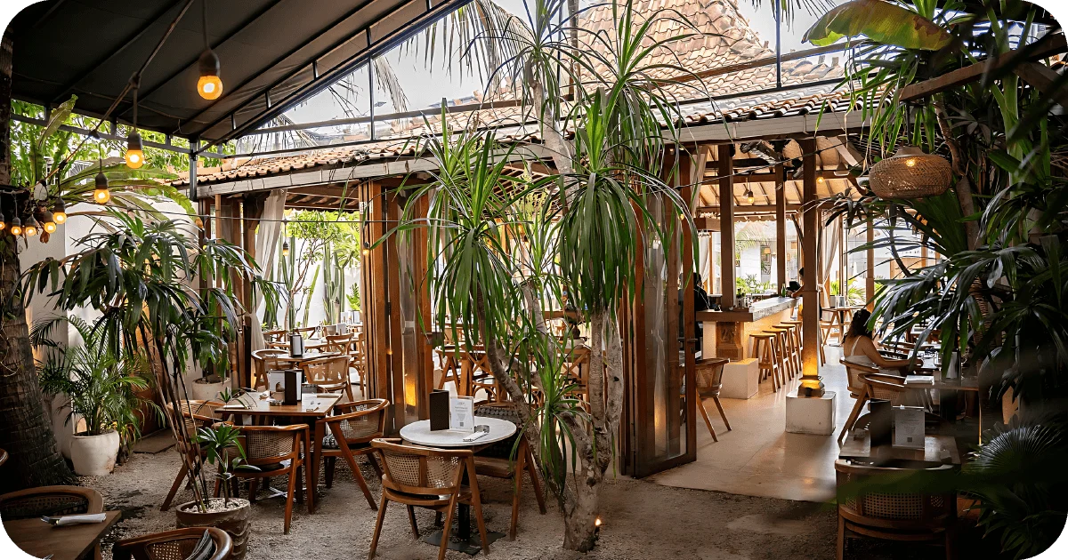 Lush semi-outdoor seating with trees, bar counter, and string lights