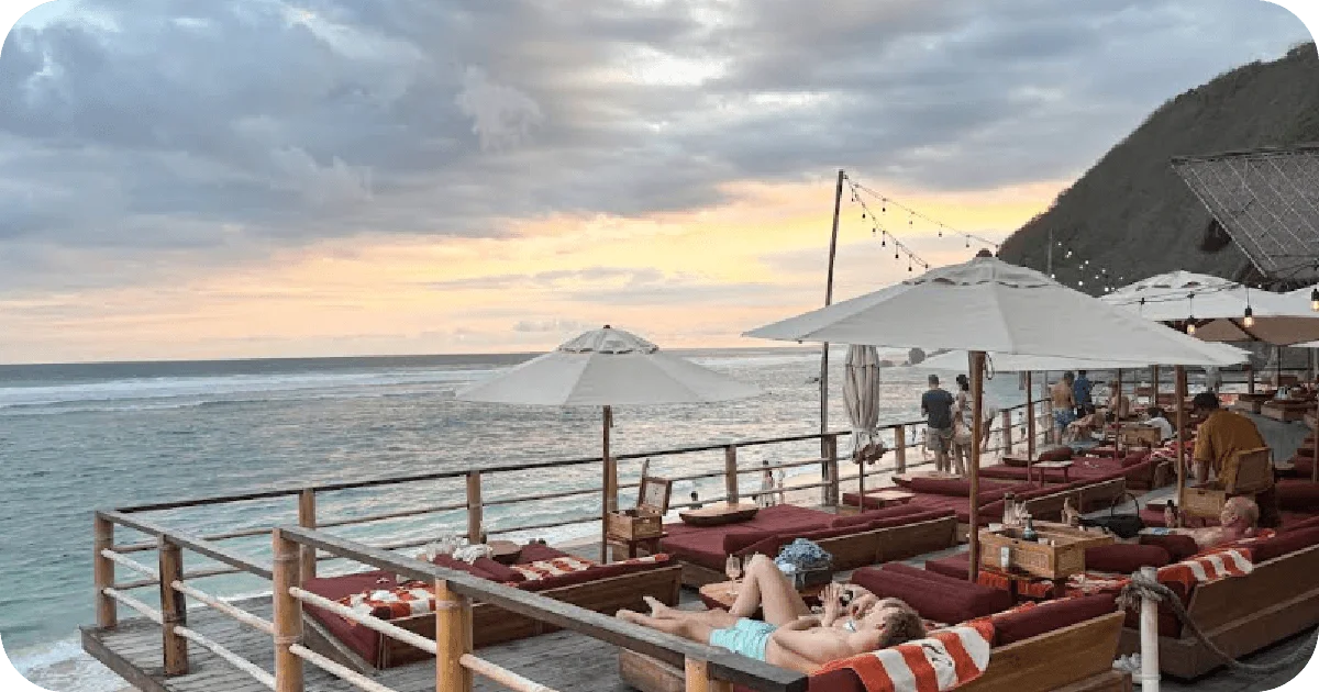 Oceanfront deck daybeds with umbrellas and string lights at sunset