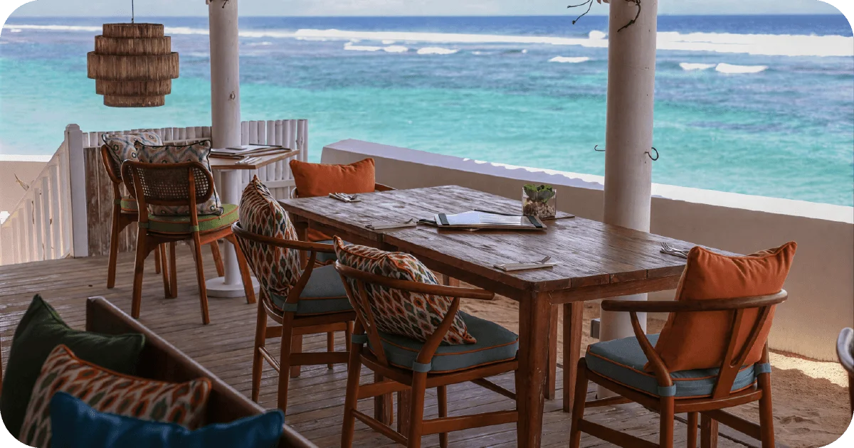 Oceanview terrace with rustic wooden tables and patterned cushioned chairs