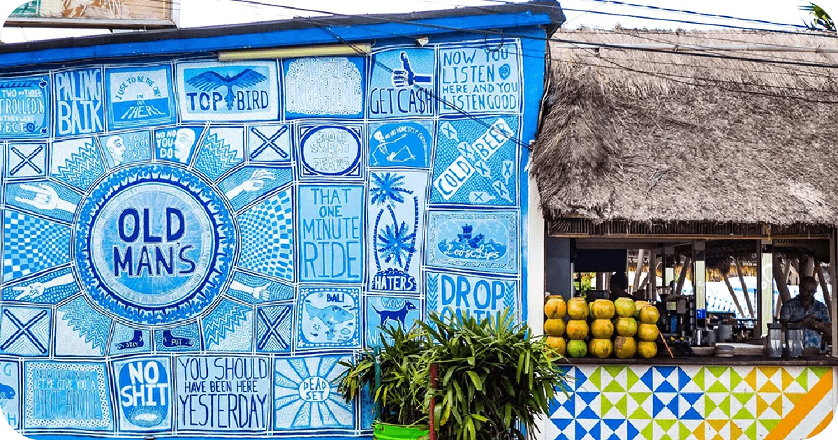 Old Man's mural exterior beside open bar with stacked coconuts