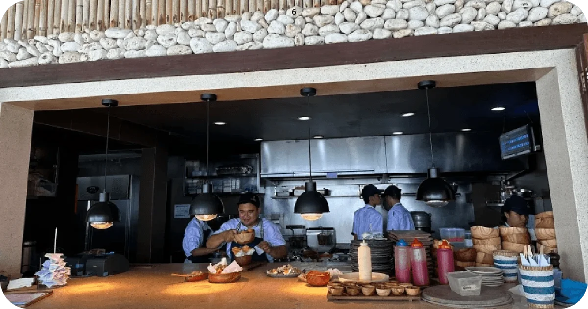 Open kitchen counter with hanging lights, wooden bowls, and staff preparing dishes