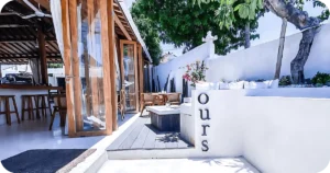 Ours side entrance with white stucco, wood panels, outdoor tables