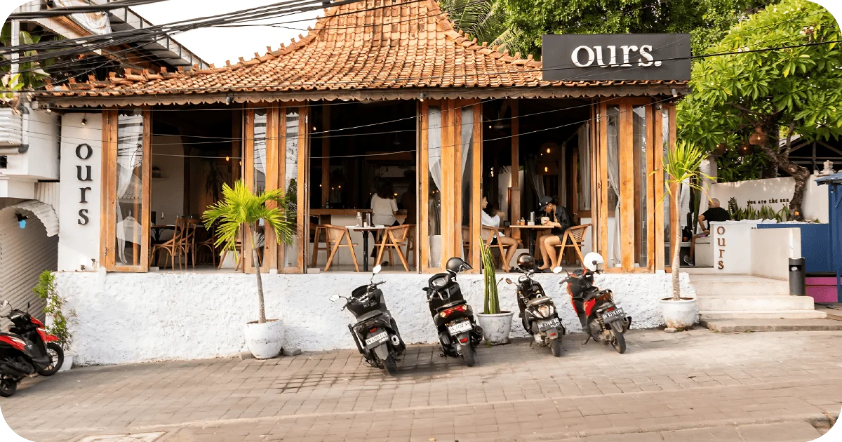 Ours streetfront facade with wood-framed windows and scooter parking