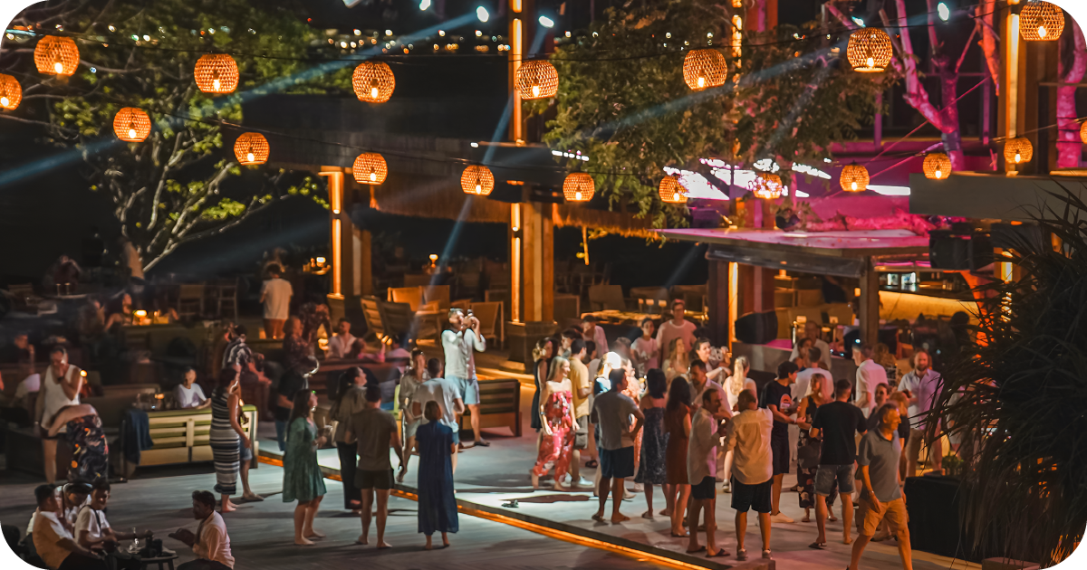 Outdoor dance floor with hanging lanterns and crowded bar at night