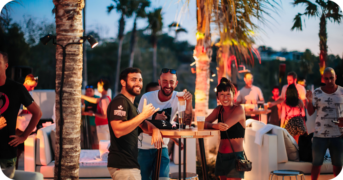 Outdoor standing tables beneath palms, guests drinking cocktails