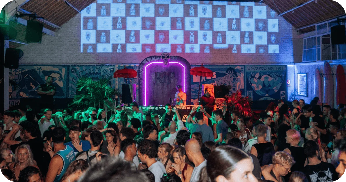 Packed dance floor with DJ booth under neon skull arch