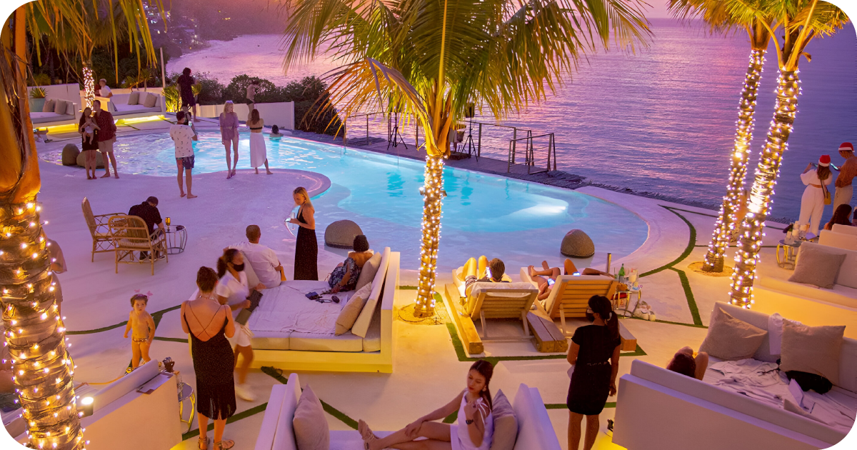 Poolside lounge at sunset with string-lit palms and sea view