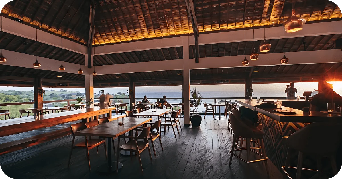 Rooftop dining with pendant lights, communal table, and ocean backdrop