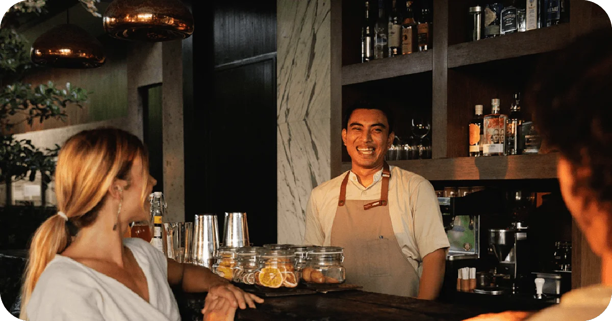 Smiling bartender at wooden back bar with spirits and citrus jars