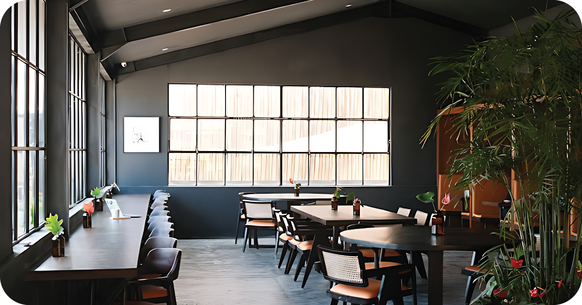 Spacious dining room with large windows, plants, and round tables