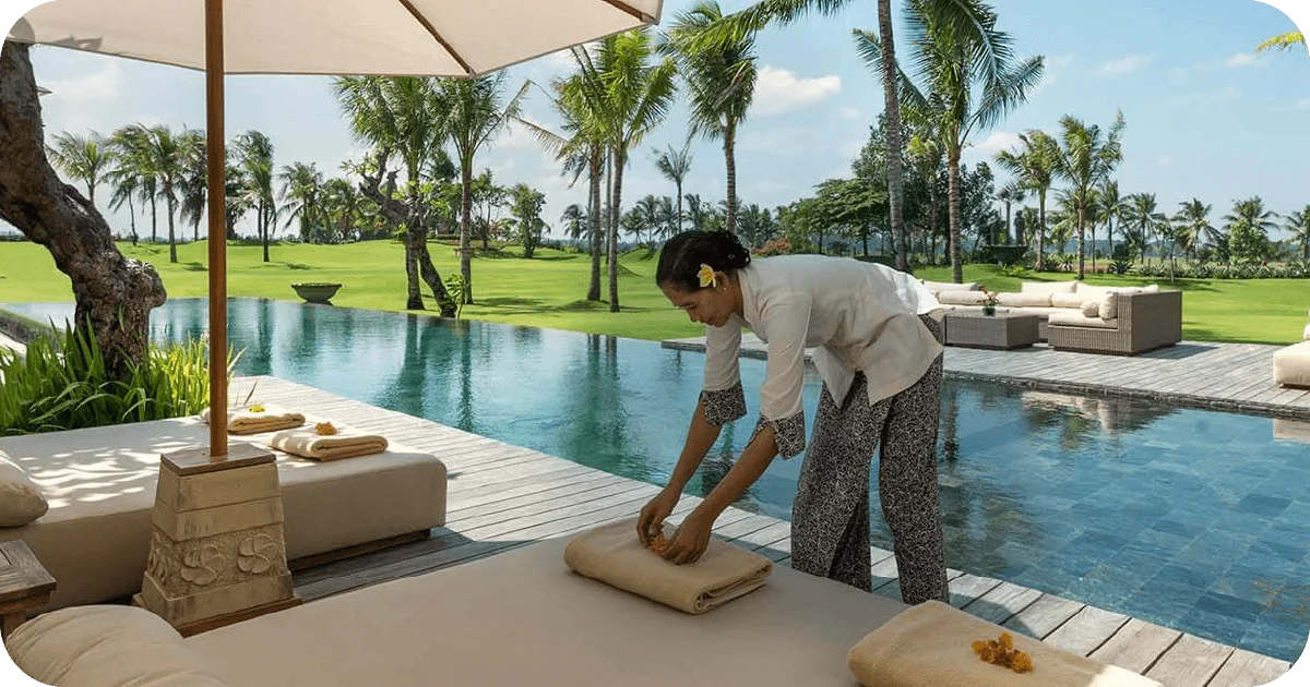 Staff preparing towels beside infinity pool, sun loungers and palm lawns