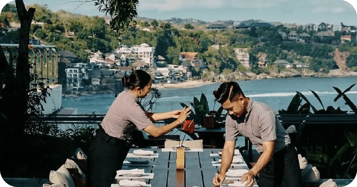 Staff setting a long outdoor table overlooking a coastal bay