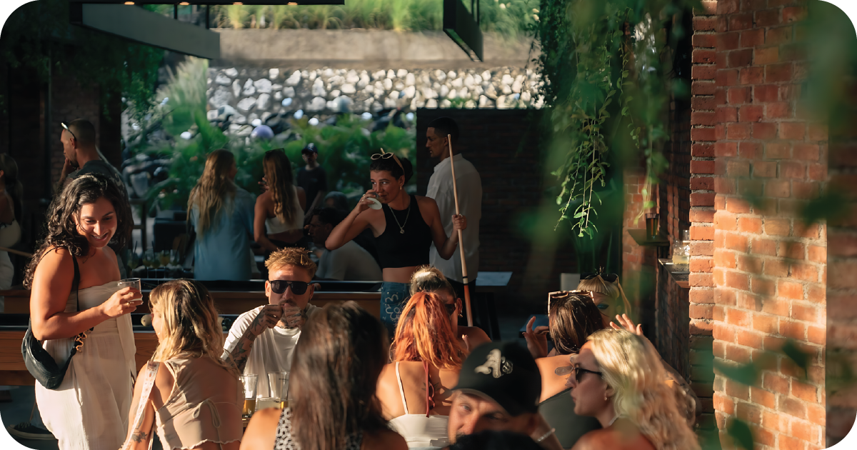 Sunlit indoor bar with brick walls, crowded tables, and pool cue