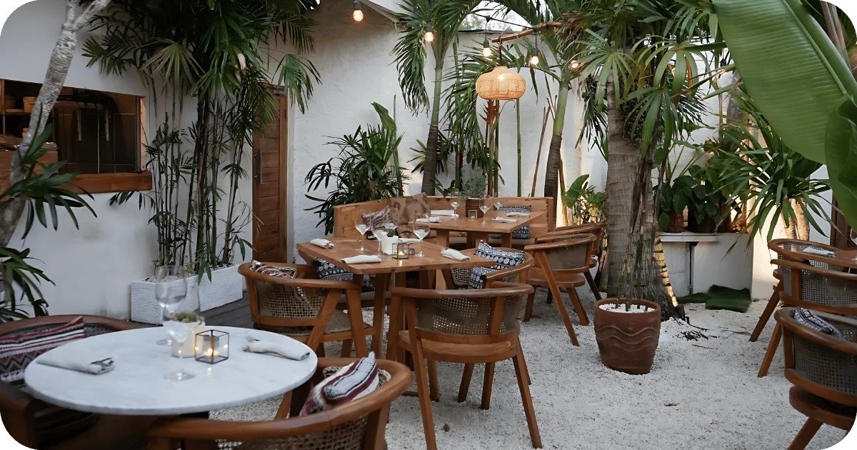 Tropical courtyard dining with wooden chairs, string lights, and candlelit tables