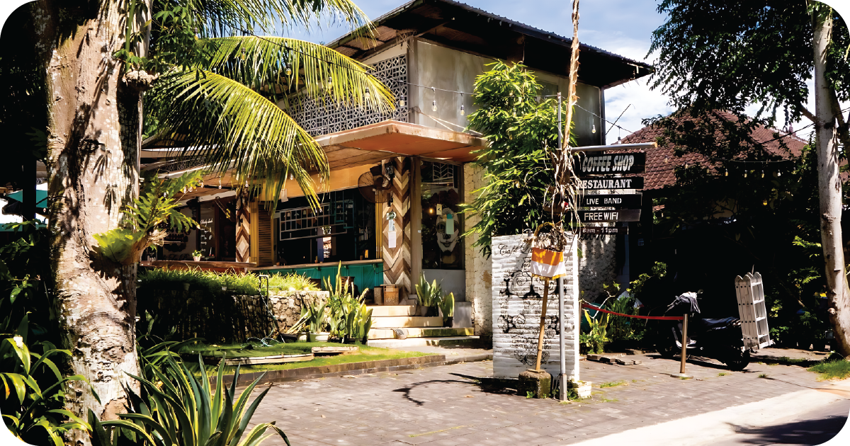 Tropical streetfront café with patio steps and “Coffee Shop” signboard