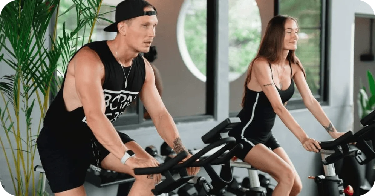 Two people riding indoor spin bikes during cardio session