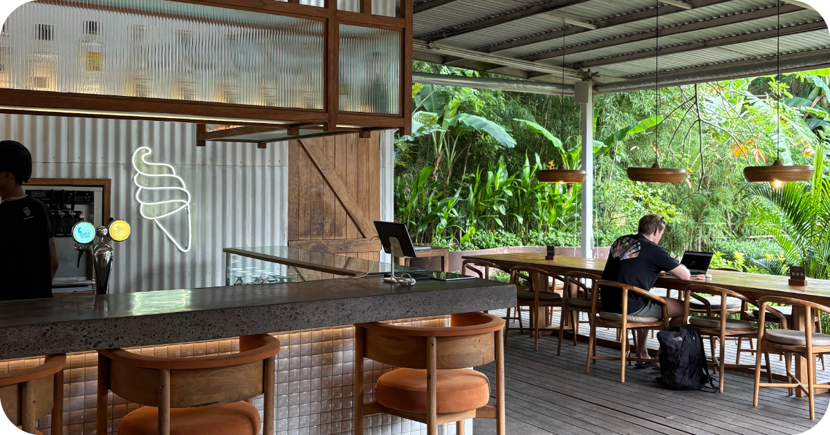 Bar with neon soft-serve sign, high stools, jungle-view communal table
