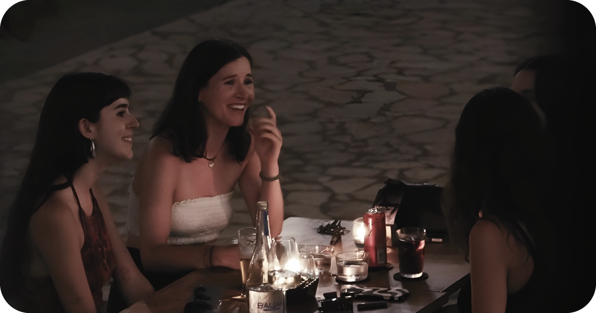 Candlelit outdoor table with cocktails and water, friends chatting