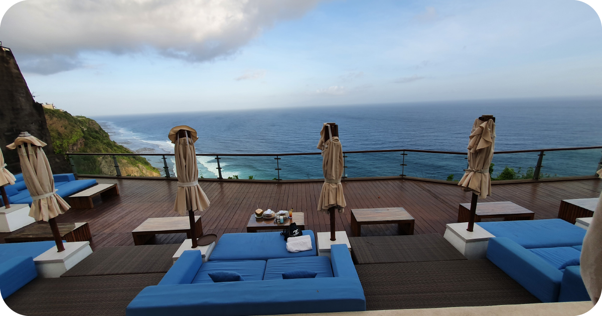 Cliffside deck with blue daybeds, closed umbrellas, and sweeping ocean view
