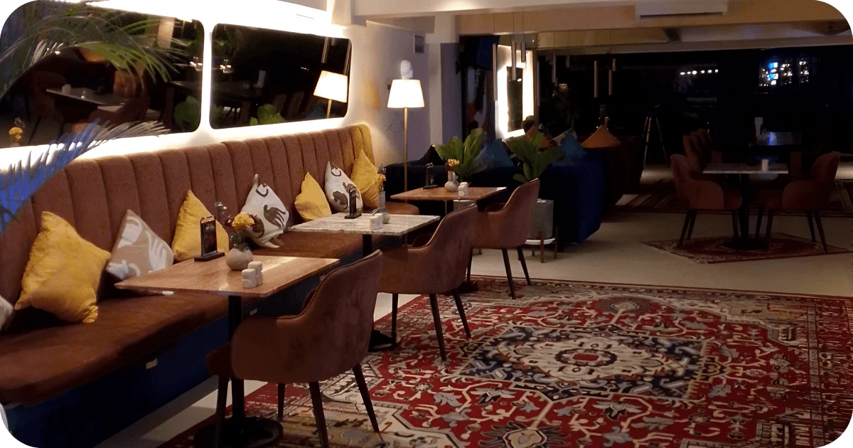 Cozy banquette seating with small tables, patterned rug, and lamps