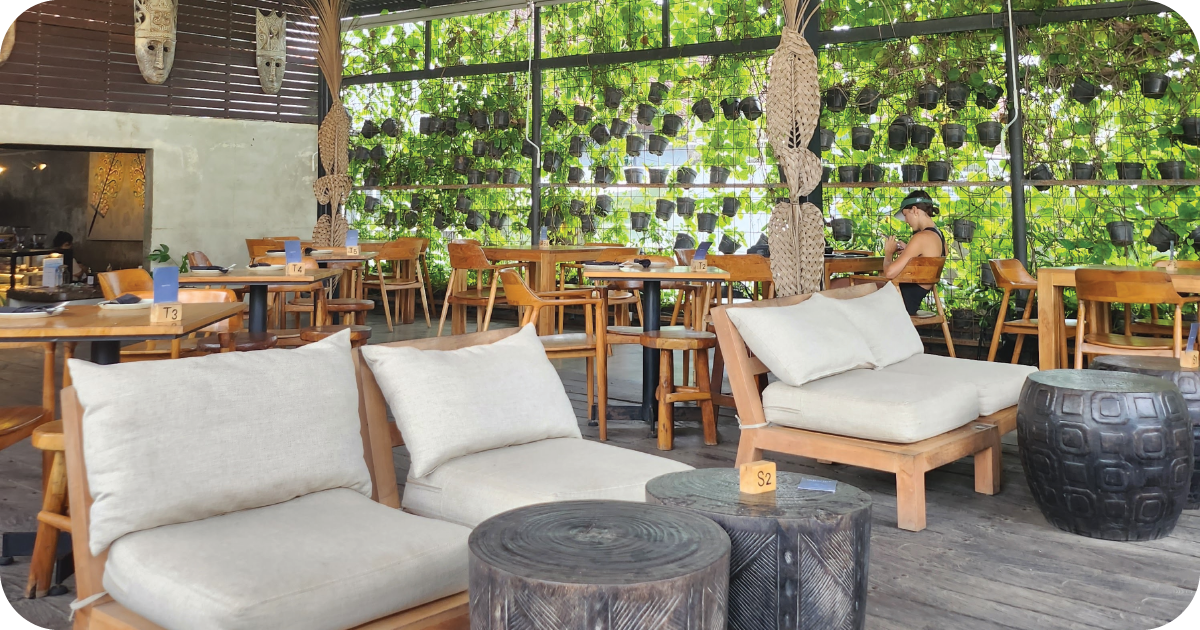 Daytime dining room with vine wall, wooden tables, cushioned lounge chairs