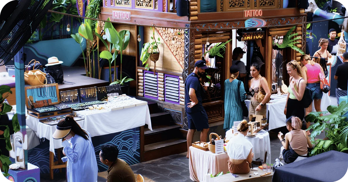 Daytime market stalls with jewelry displays beside tattoo booth
