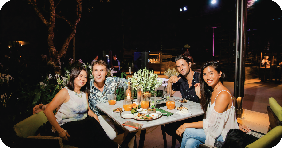Friends dining outdoors at night with cocktails and shared plates
