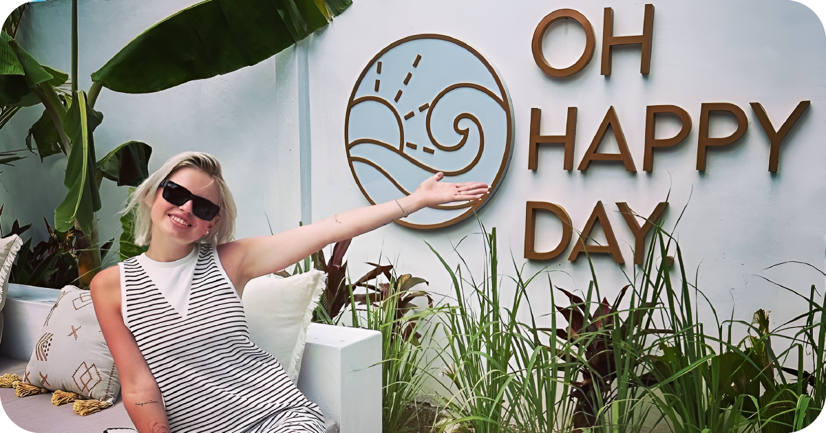Guest posing beside OH HAPPY DAY sign and tropical foliage