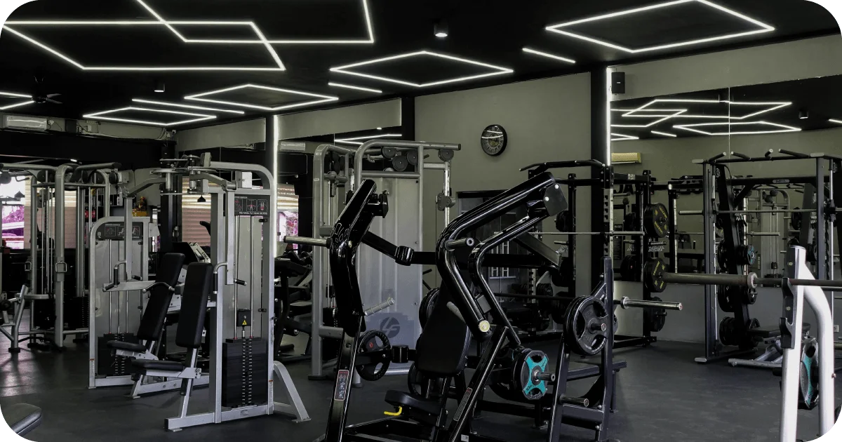 Gym floor packed with machines under geometric LED ceiling