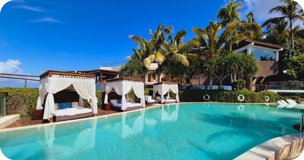 Infinity pool with curtained cabanas and palm trees under blue sky