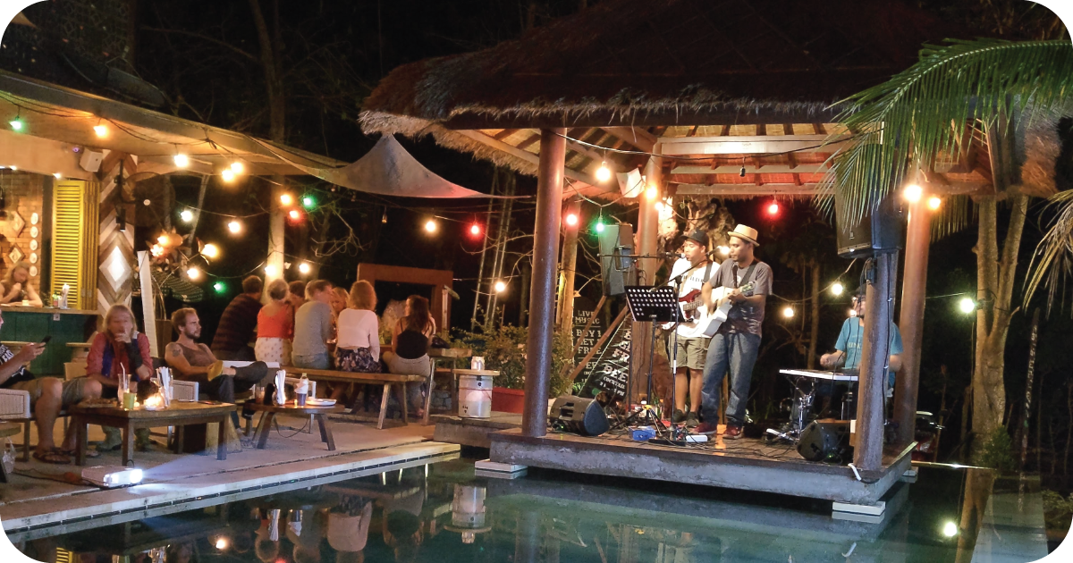 Live band performing on gazebo stage by pool, string lights overhead