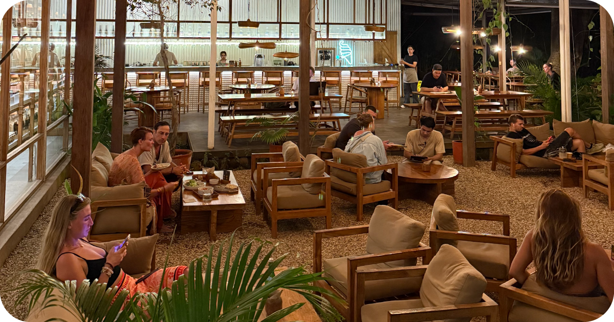 Nighttime lounge with cushioned chairs facing open bar and kitchen