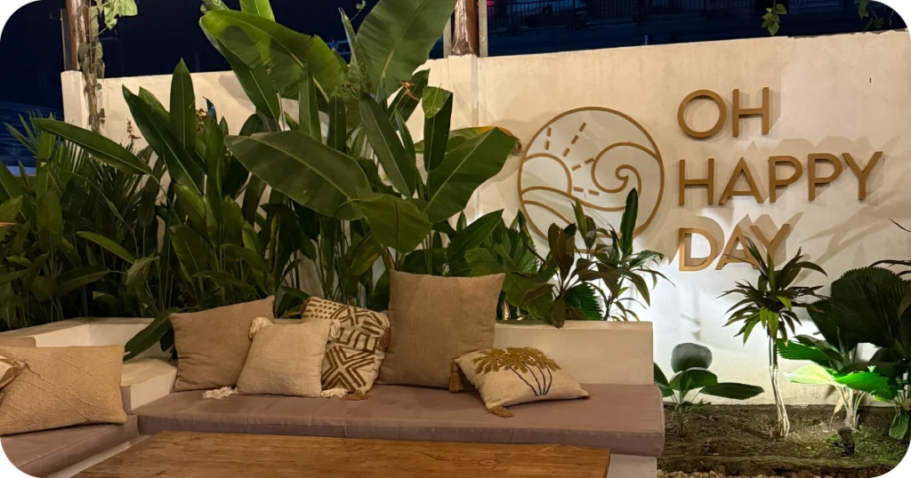 Ohana Restaurant & Bar Bali: OH HAPPY DAY wall sign above cushioned bench and tropical plants
