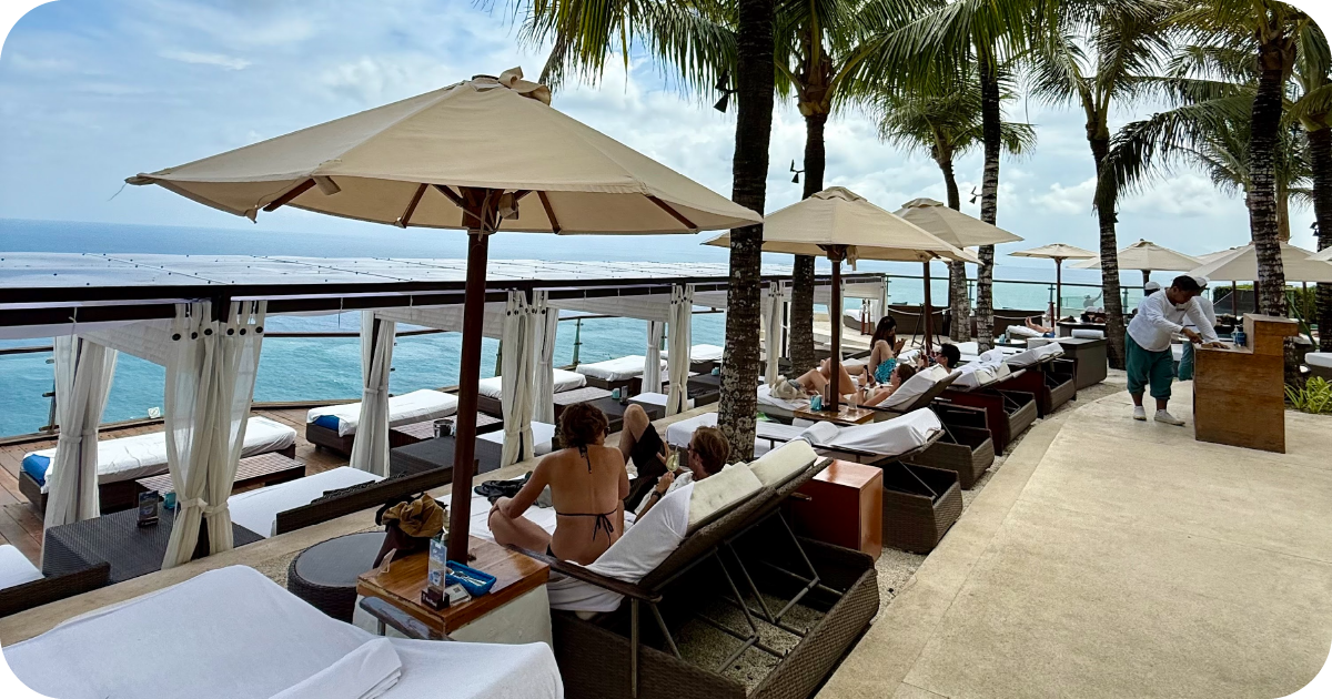 Oceanfront terrace with rows of cushioned loungers, umbrellas, and palm trees
