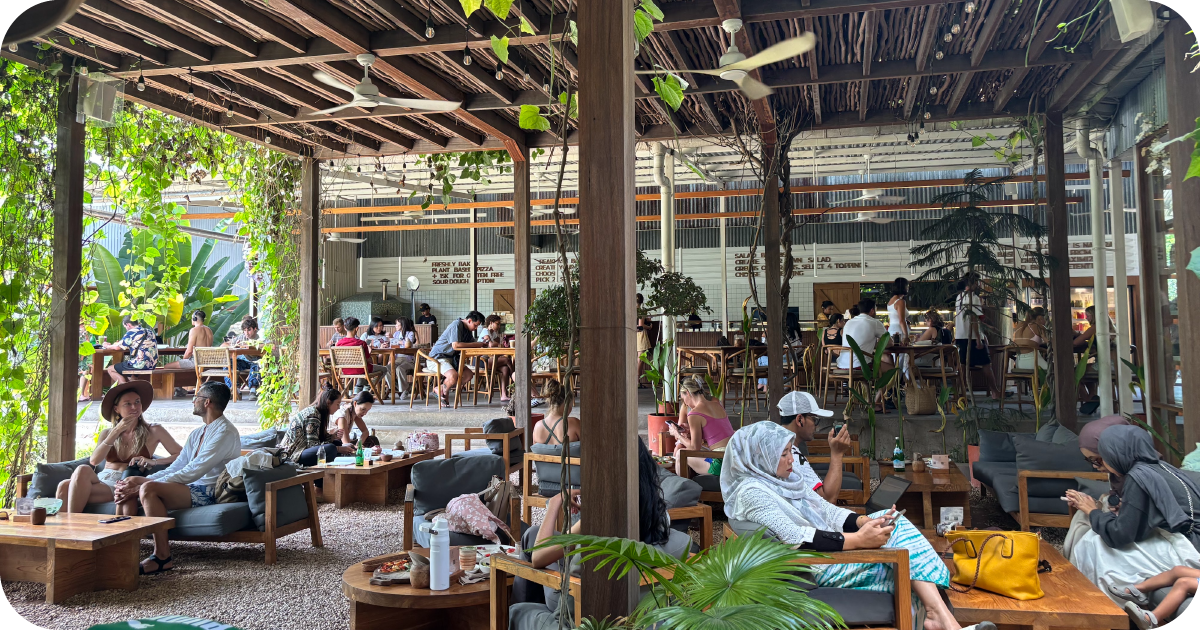 Open-air lounge seating with wooden tables, greenery, and ceiling fans